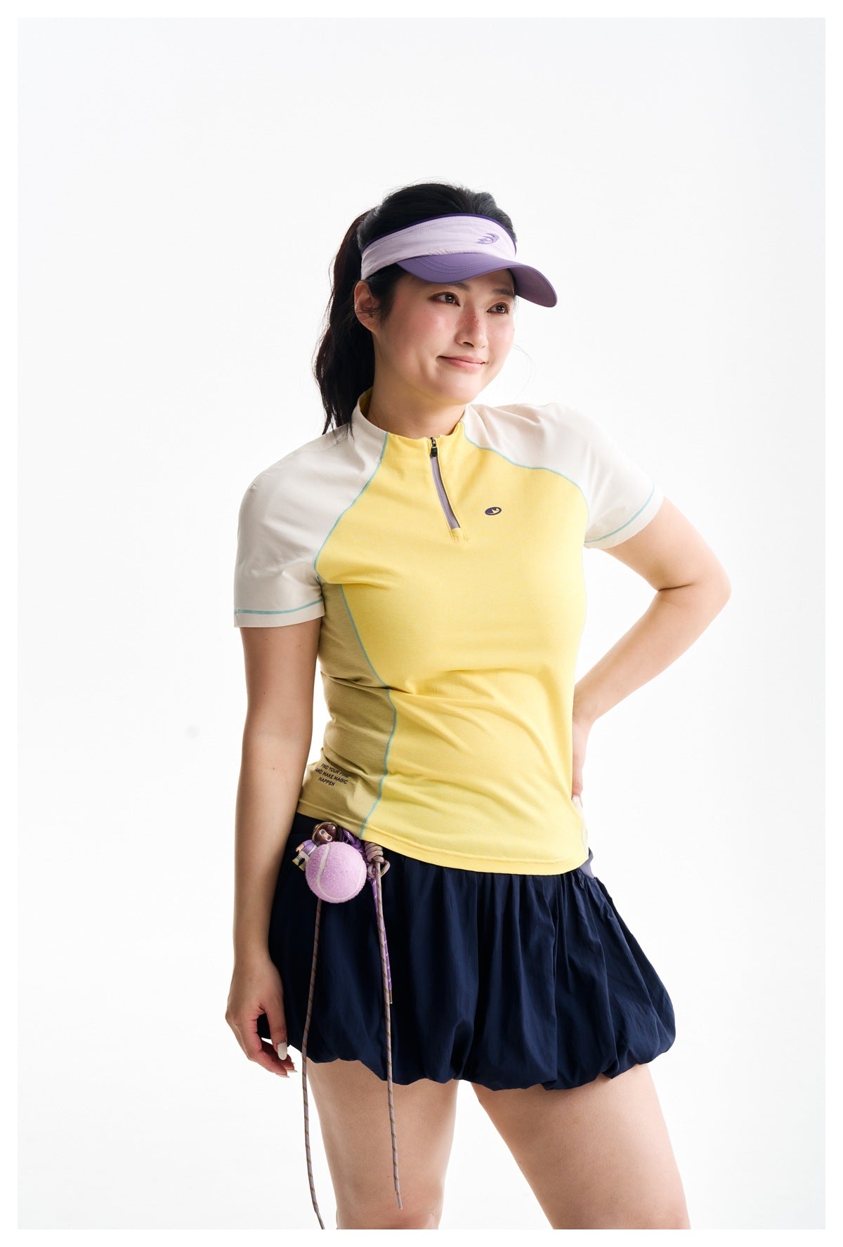 Model wearing a yellow and ivory zip-neck athletic top, navy bubble skirt and purple visor.