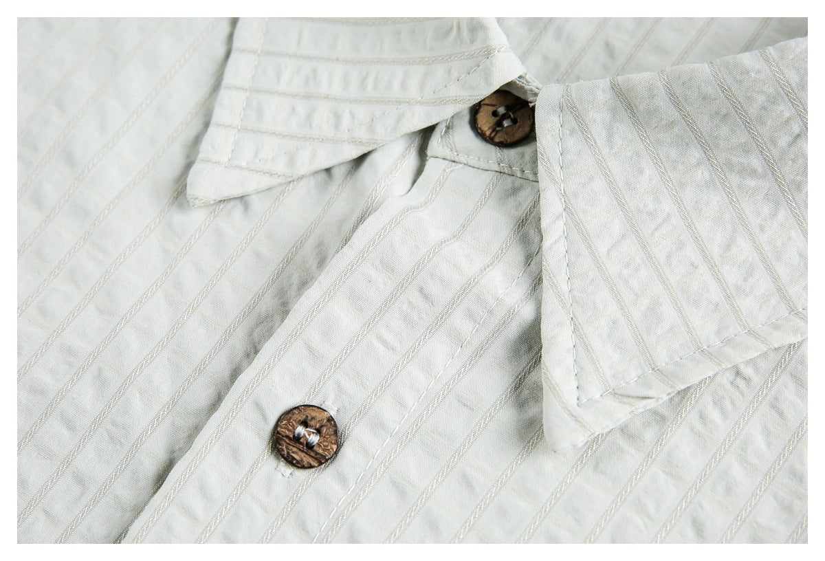 Close-up of a white shirt collar, placket, and brown buttons against textured vertical stripes.