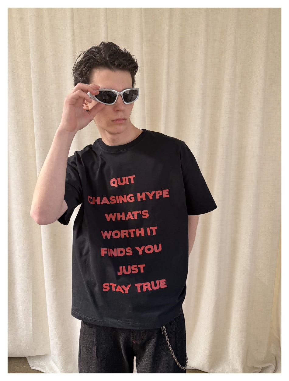 Close view of a model wearing a black T-shirt with bold red text and white-framed sunglasses.