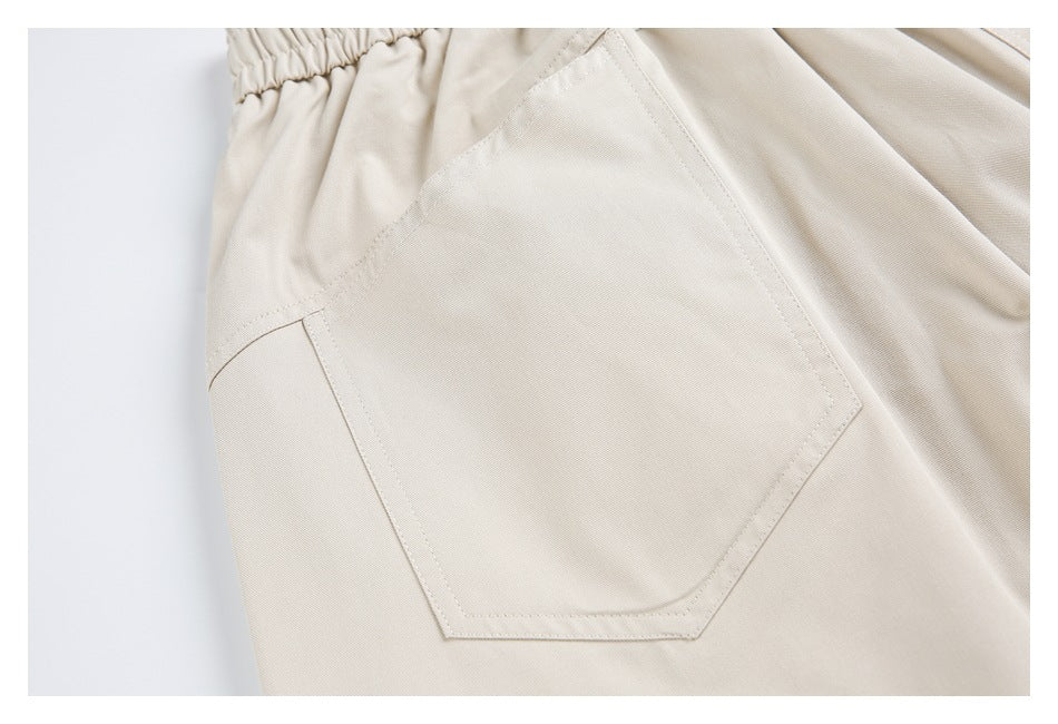 Close-up of light beige trousers showing a large stitched pocket and part of an elastic waistband.