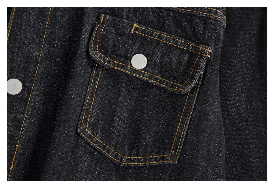 Close-up of a dark denim jacket flap pocket with silver snap and contrast gold stitching.