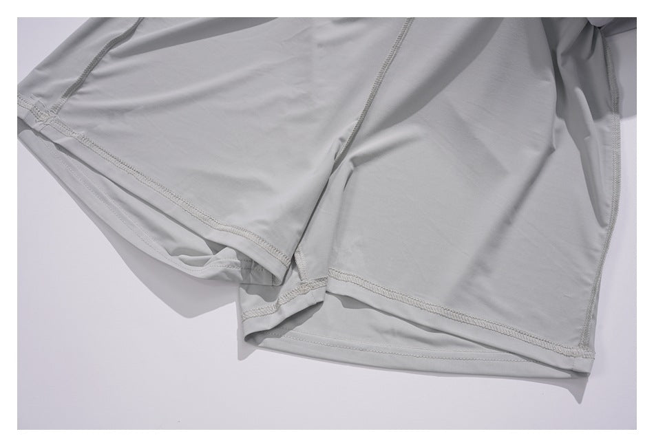 Close-up of a light gray garment laid flat, showing overlapping fabric panels and stitched hems.