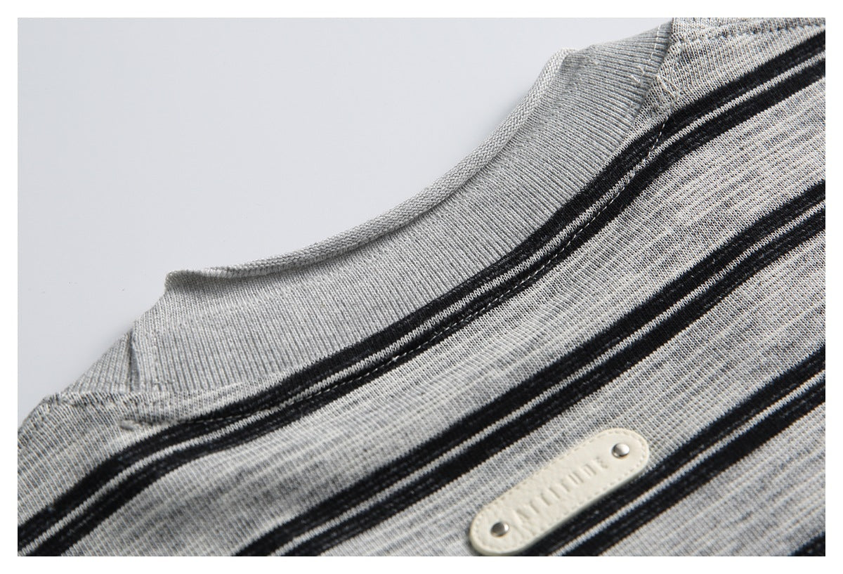 Close-up of a gray-and-black striped knit garment neckline and a small cream-colored metal-studded patch.