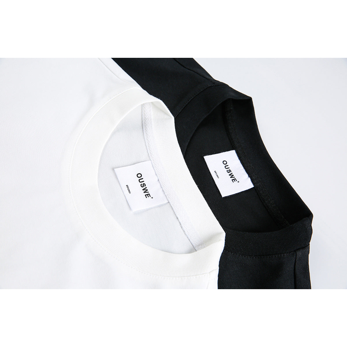 Close-up of white and black sleeveless tops showing ribbed crew necks and sewn-in neck labels.