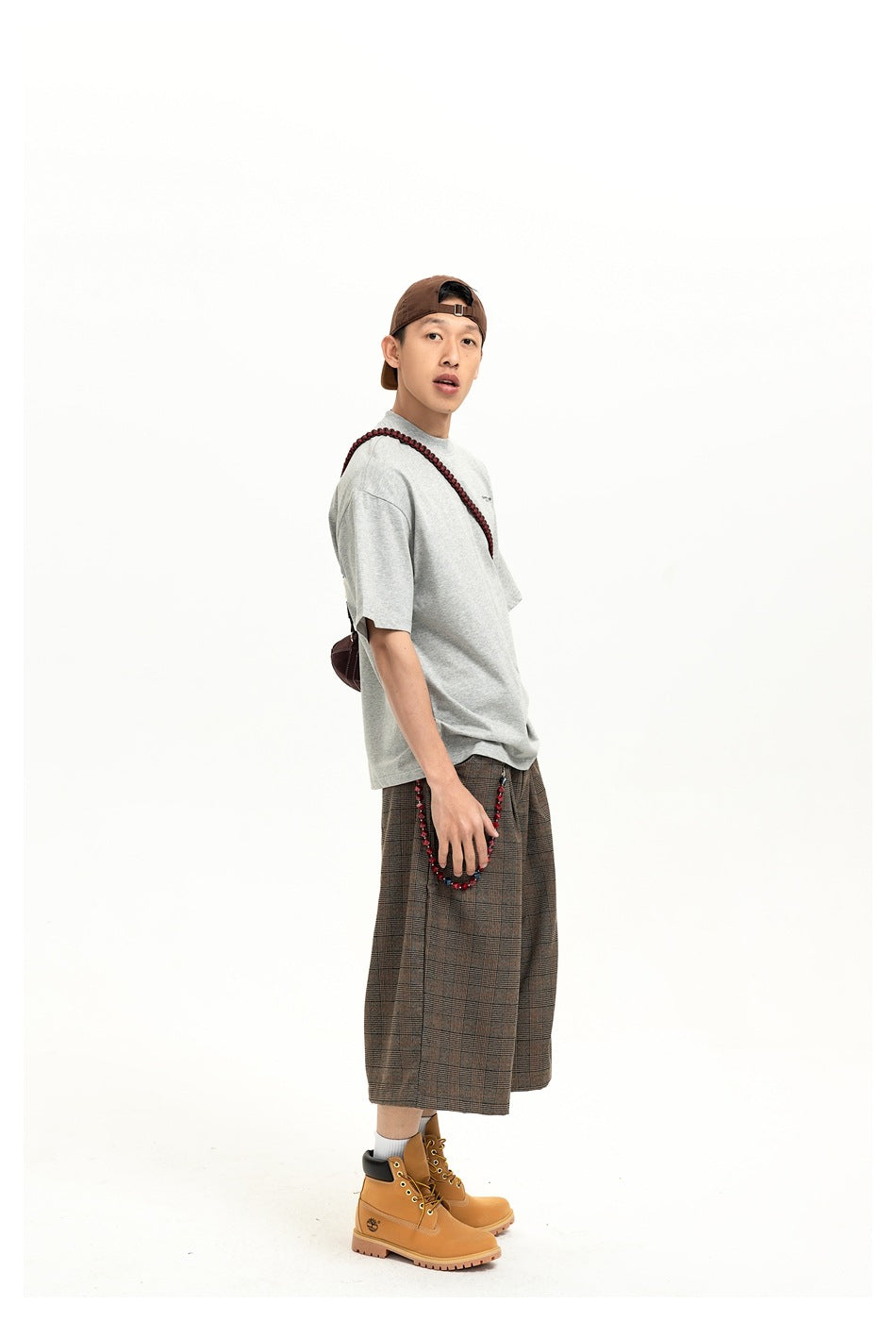 Side view of a model wearing a light gray oversized T-shirt and brown plaid shorts.
