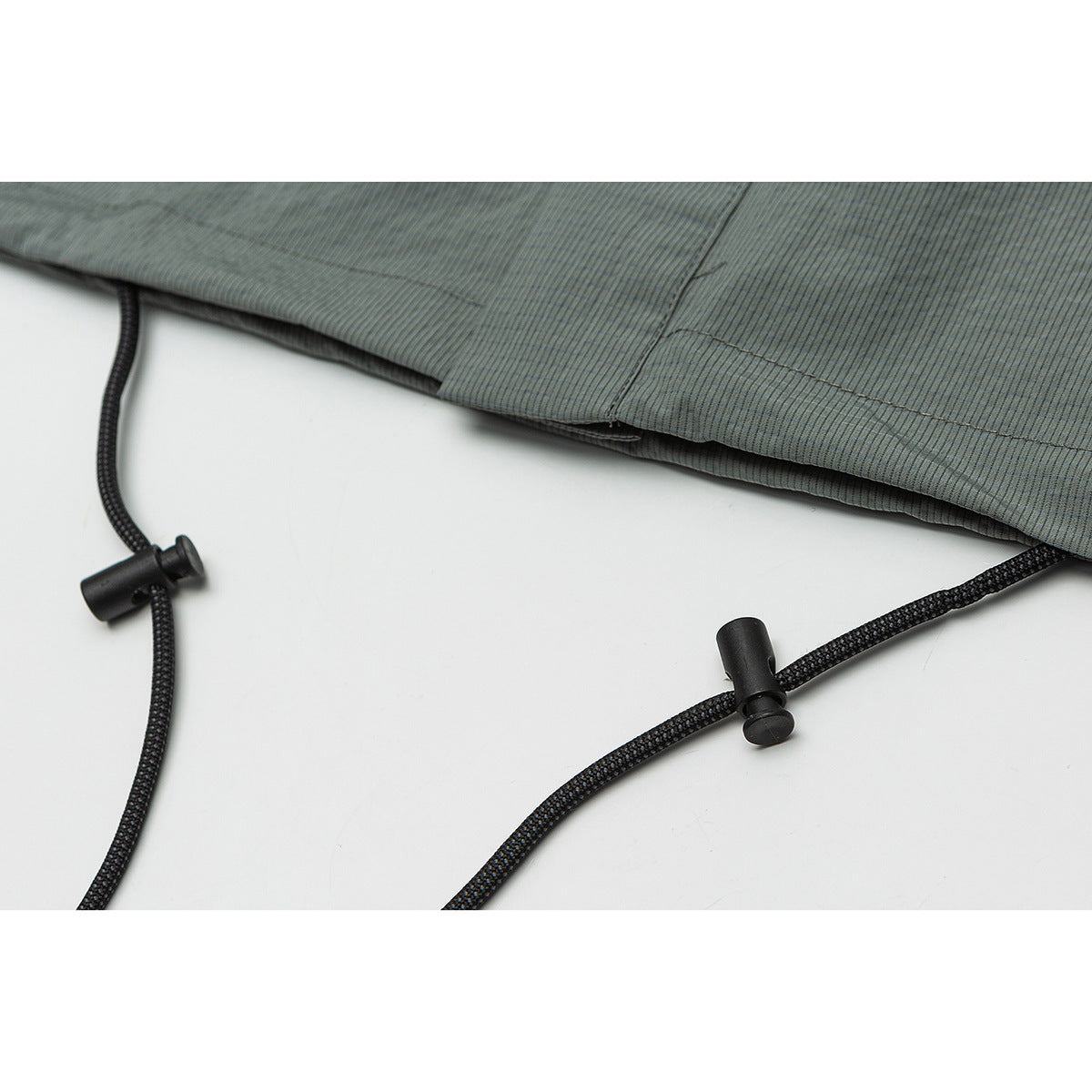 Close-up of a gray-green shirt hem with black adjustable drawcords and cord locks.