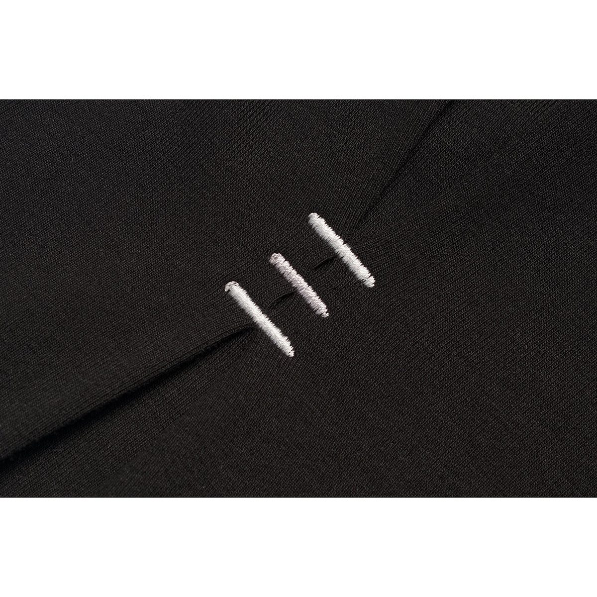 Close-up of three short white embroidered stitches on black fabric.