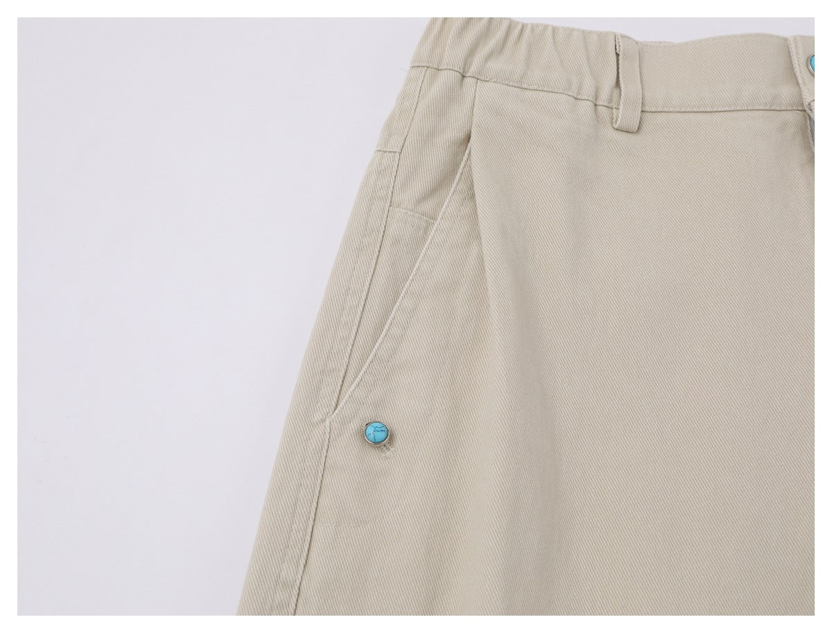 Close-up of beige trousers showing the waistband, belt loop, and turquoise side button.