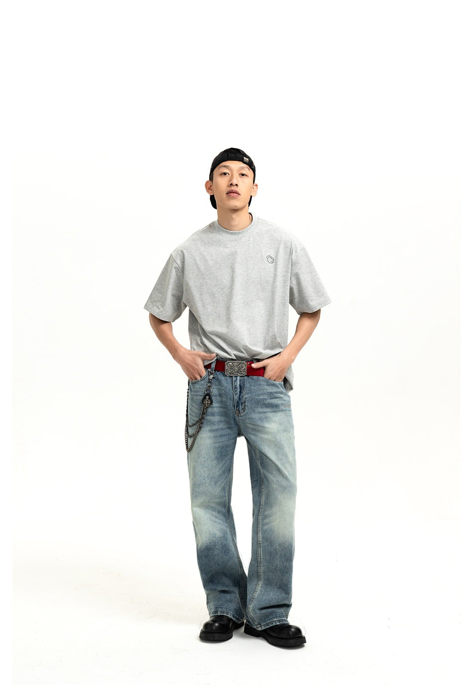 Model wearing faded blue wide-leg jeans with a gray T-shirt, red belt, wallet chain and black boots, front view