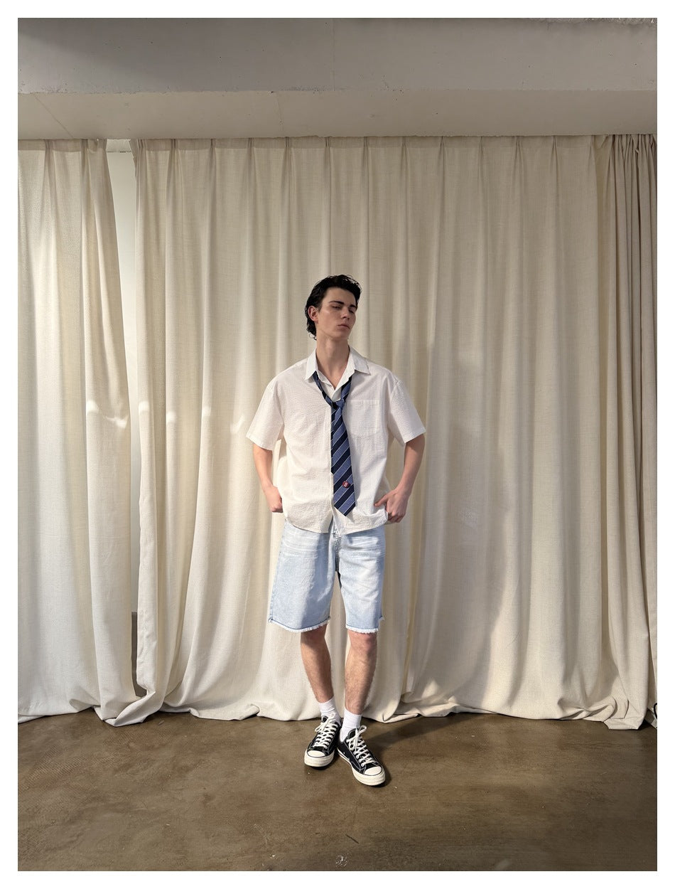 Full-length front view of a model in a white short-sleeve shirt, striped navy tie and light denim shorts.