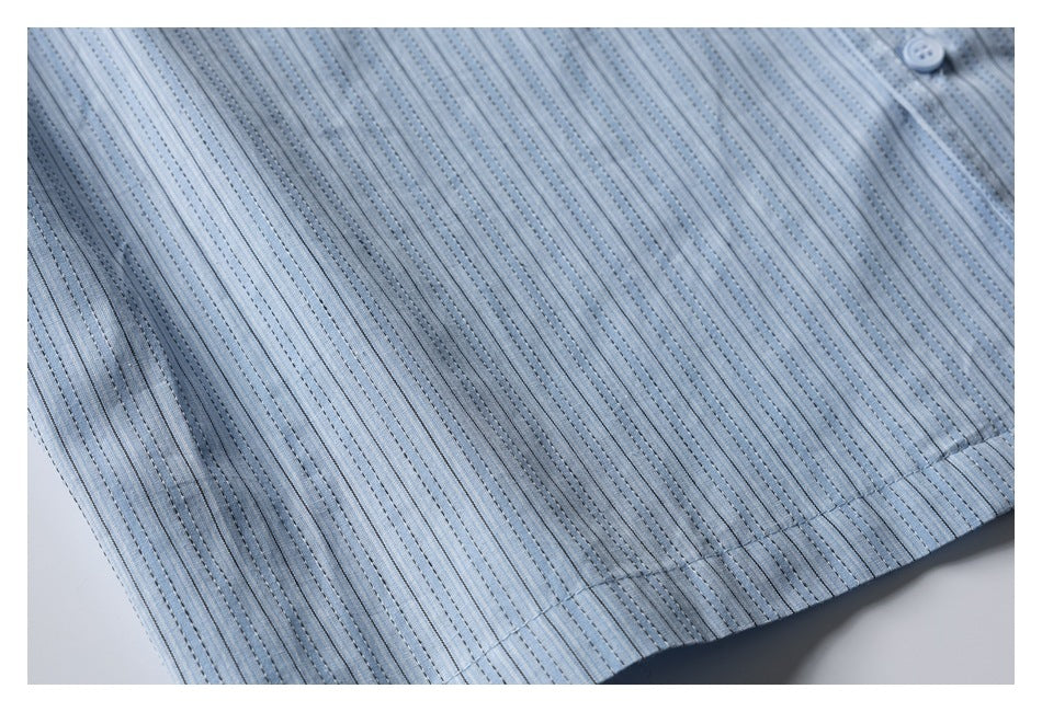 Close-up of the light blue striped shirt fabric, button, and stitched hem.