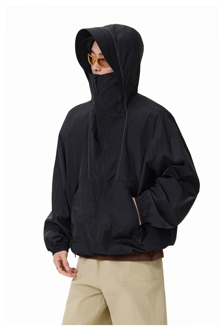 Model wearing a black hooded jacket with a full front zipper, high face-covering collar and elastic cuffs.