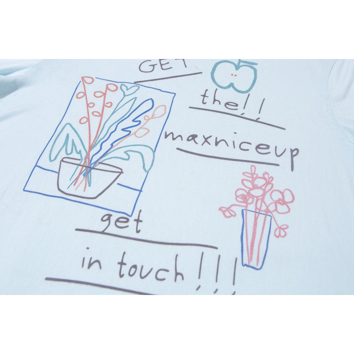 Close-up of a pale blue shirt's colorful hand-drawn floral graphic and English lettering.