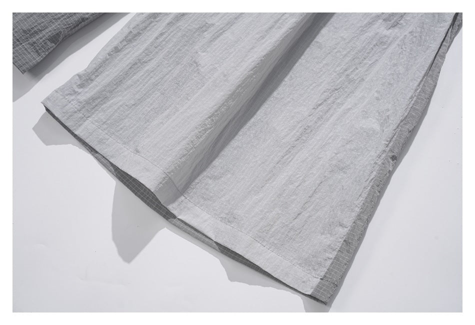 Close-up of a stitched hem on a light gray garment panel, with a darker grid-patterned layer beneath.