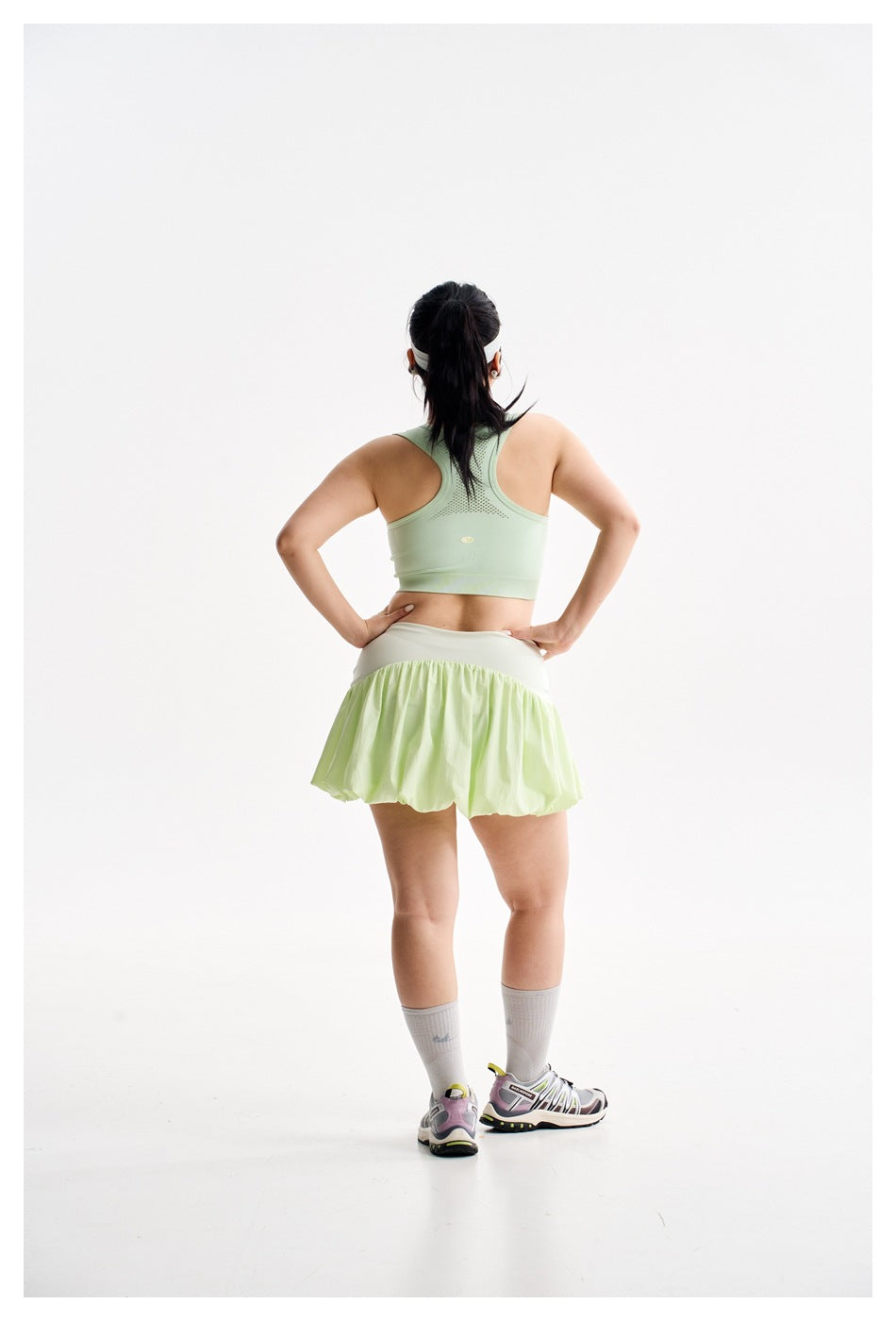 Rear view of a model wearing a pale mint sleeveless crop top and light green bubble-hem tennis skirt.