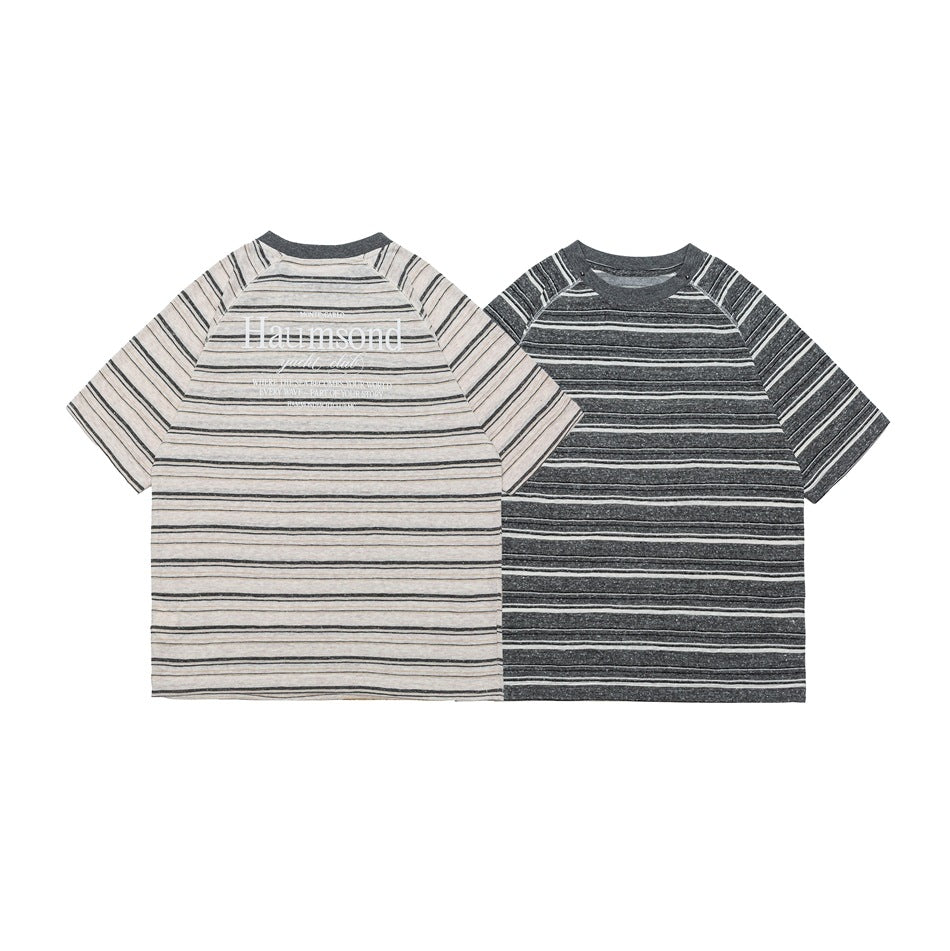 Two short-sleeve striped shirts laid flat, one cream and one charcoal gray; the cream shirt has a chest print.