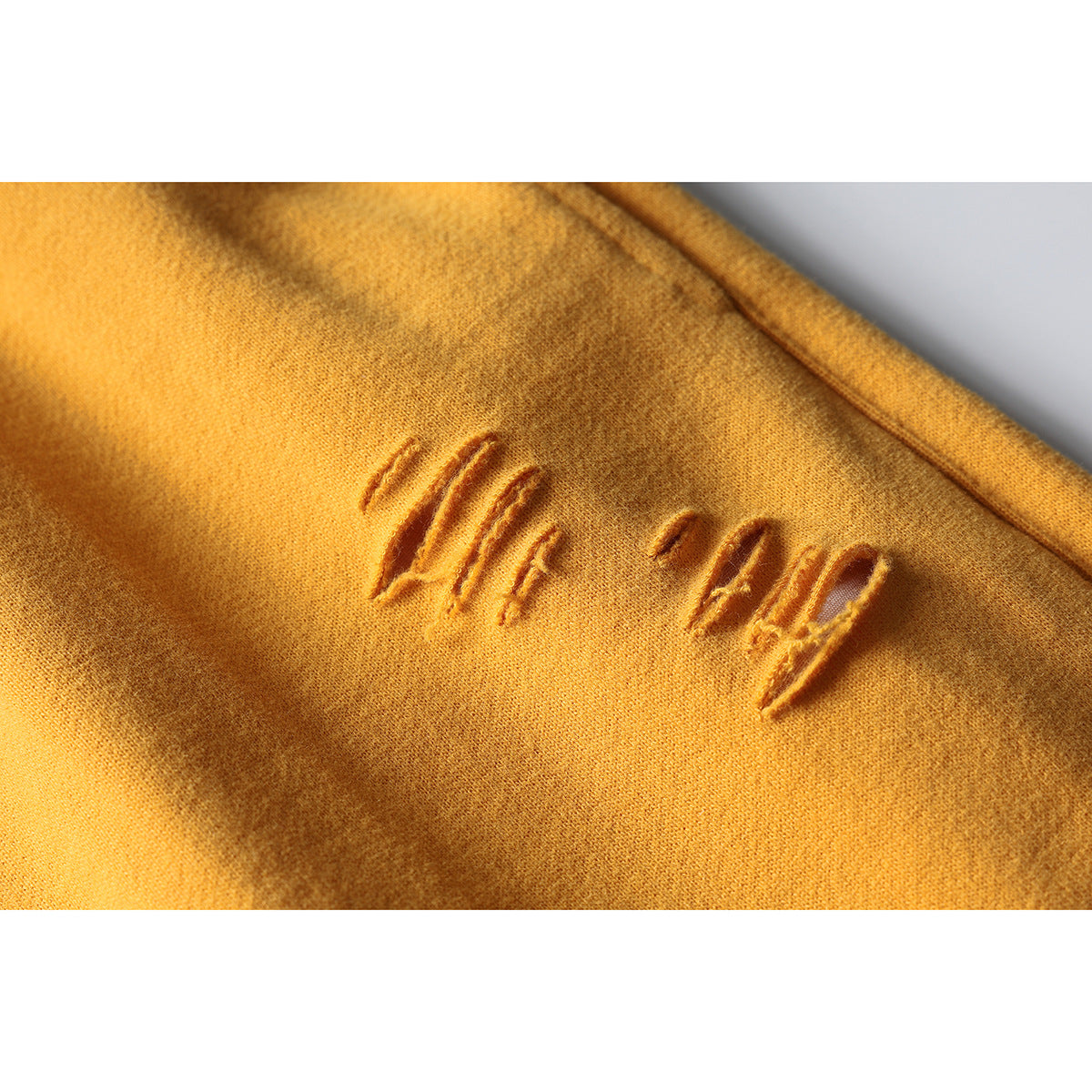 Close-up of mustard-yellow shorts with several small distressed openings in the fabric.