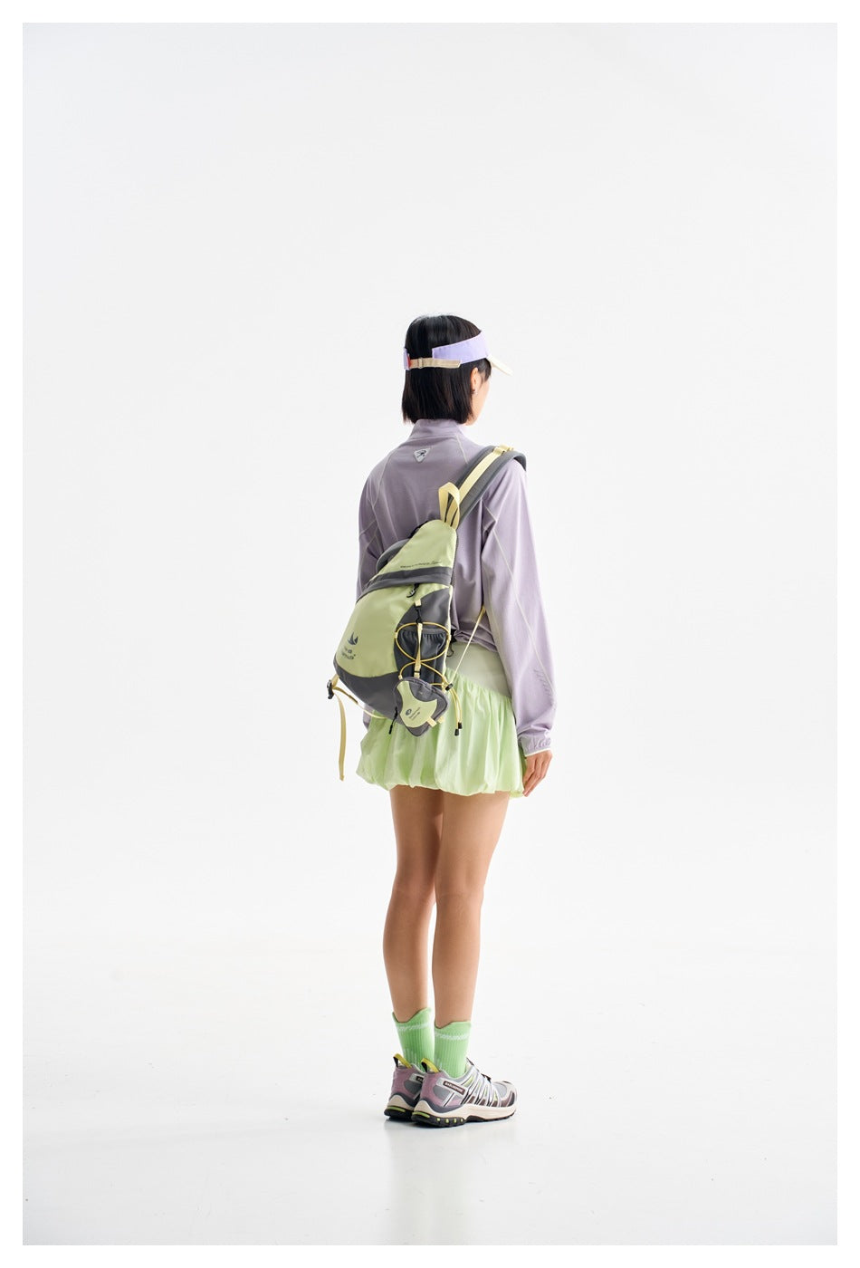 Rear view of a woman wearing a lavender top and pale green skirt with a light green backpack.