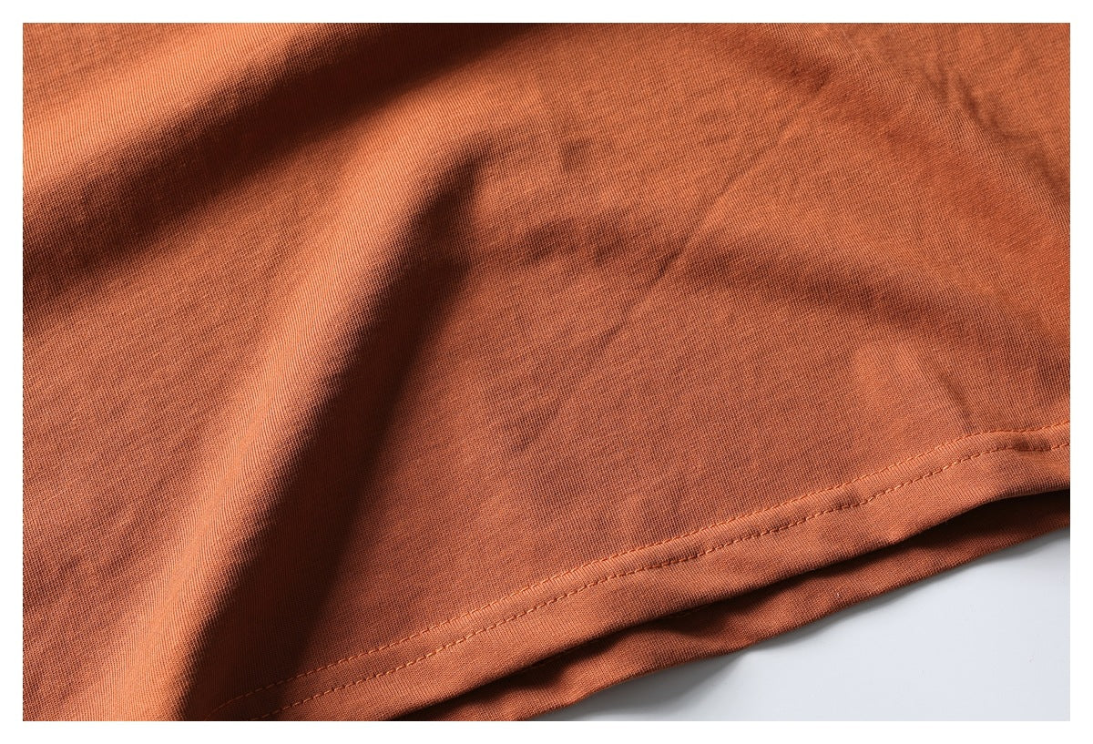 Close-up of the rust-orange garment's stitched hem and smooth fabric.