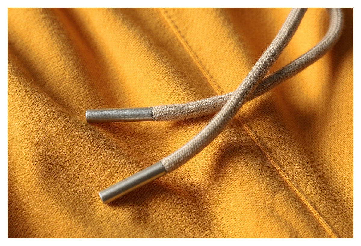 Close-up of a mustard garment with two gray braided drawstrings and metal tips.