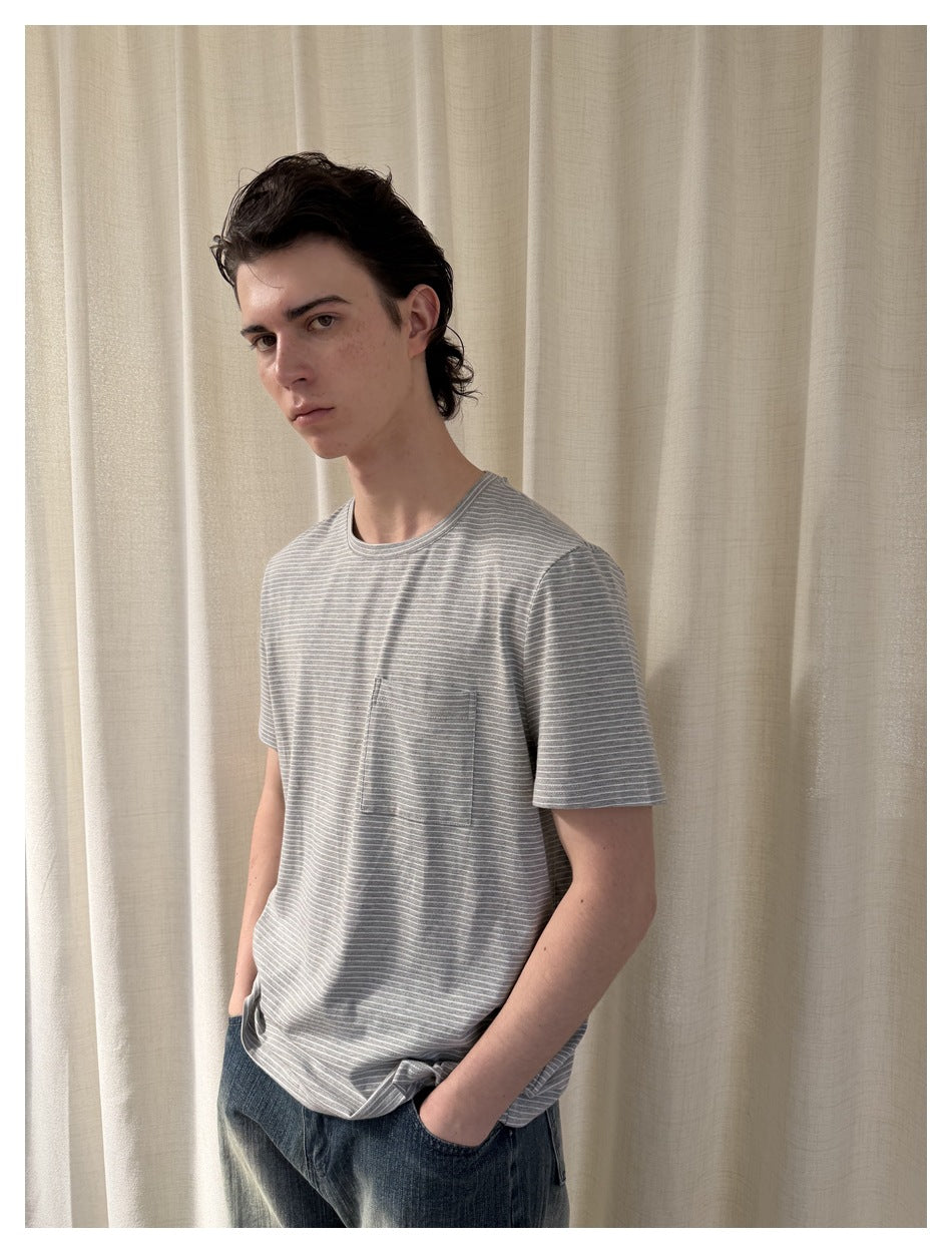 Model in gray striped crew-neck T-shirt with chest pocket, hands in jeans pockets, seen from three-quarter view