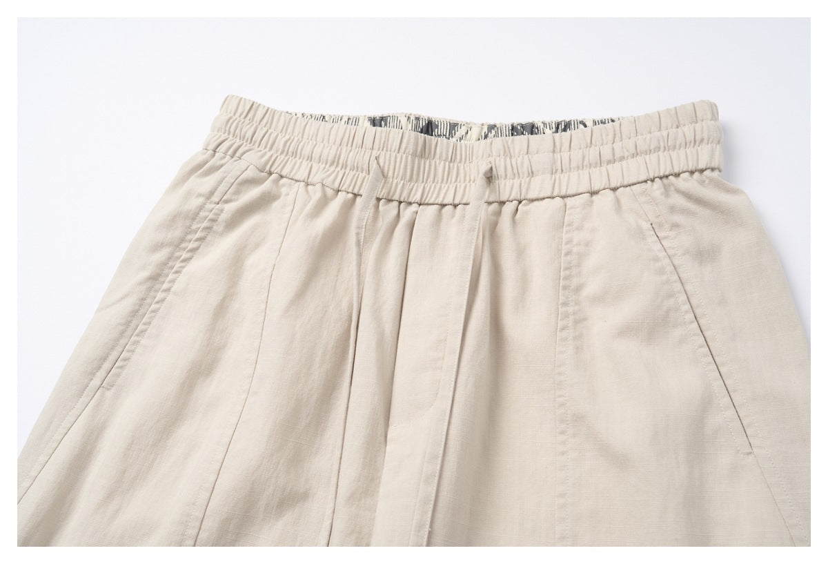 Close-up of the front of light beige shorts, showing the elastic waistband, pleats and angled pockets.