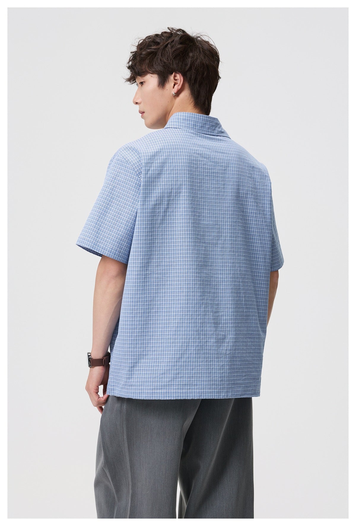 Back view of model wearing blue check short-sleeve collared shirt with gray trousers