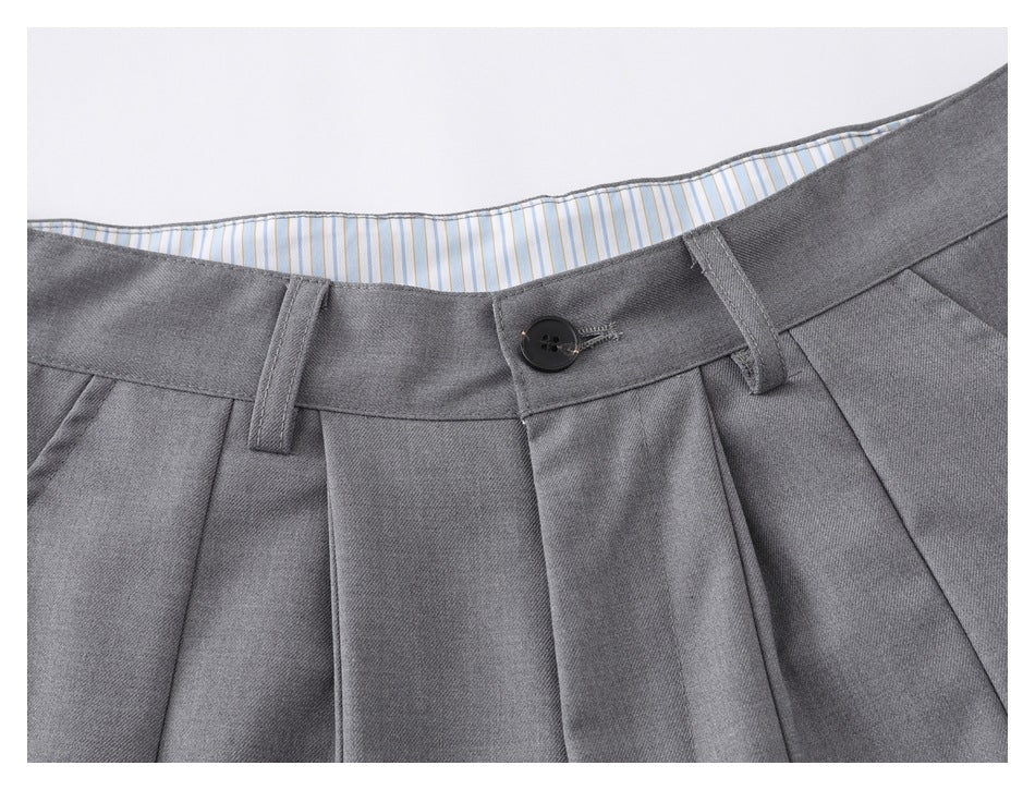 Close-up of gray shorts' front waistband, black button, pleats, and striped inner lining.