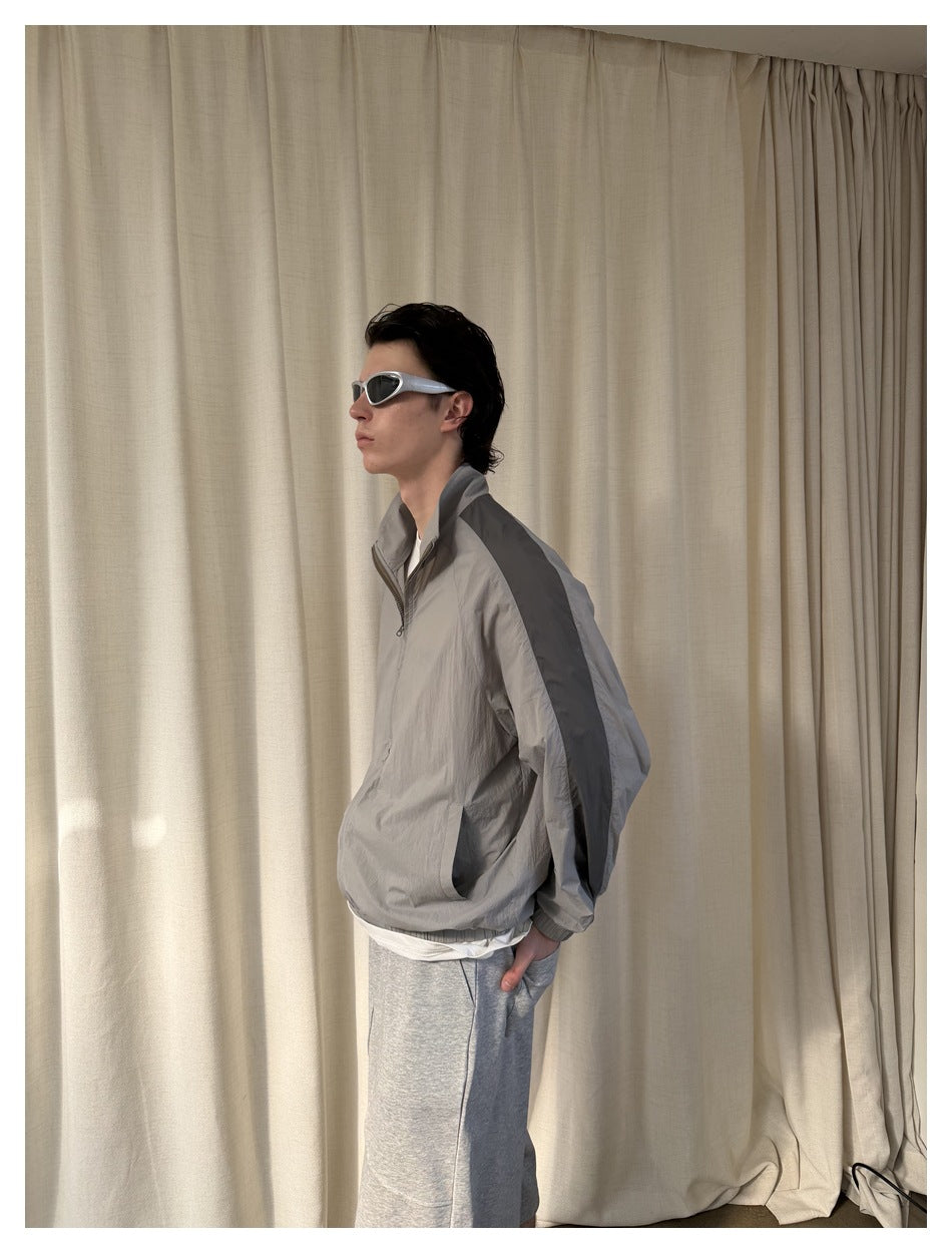 Side view of a model wearing a loose light gray jacket with dark shoulder stripes and a raised collar.