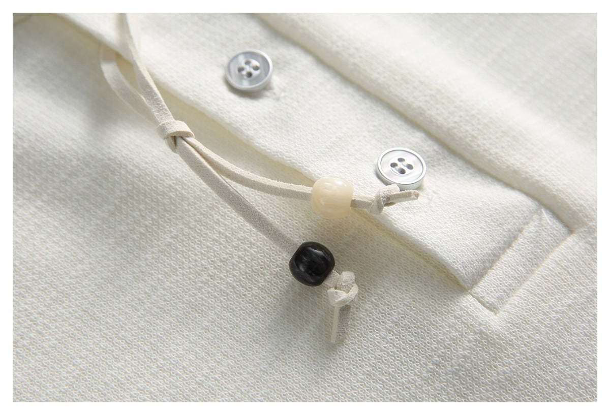 Close-up of ivory knit fabric with two buttons and a cord tie finished with light and dark beads.