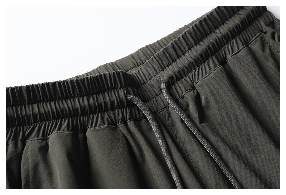 Close-up of dark olive pants with a gathered elastic waistband and matching drawstrings.