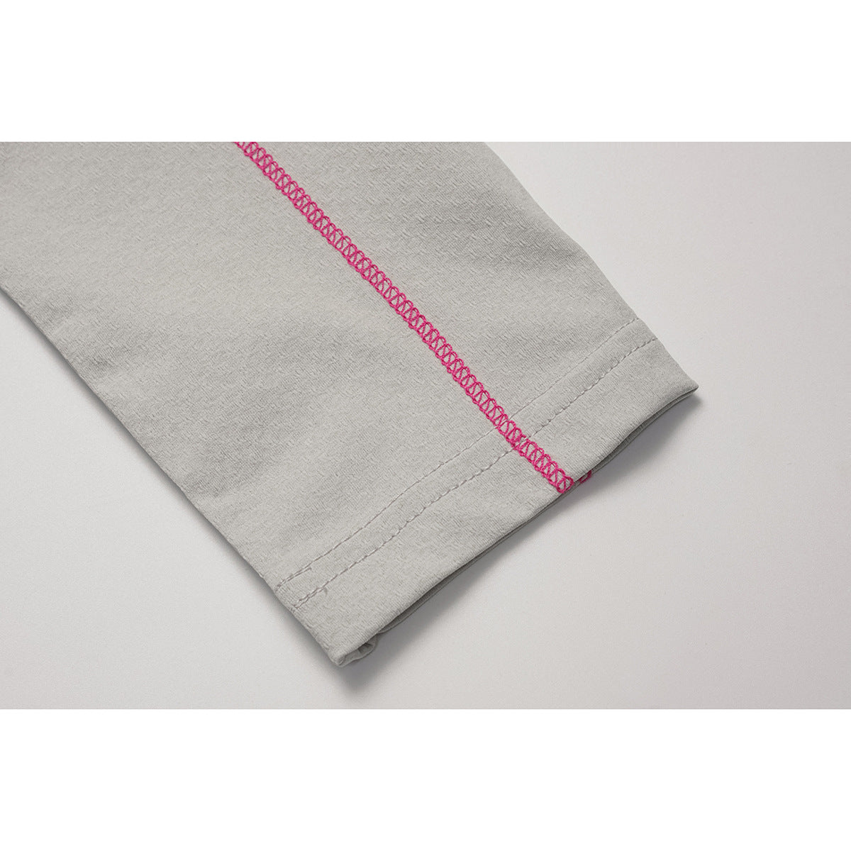 Close-up of a light gray sleeve cuff with prominent pink overlock stitching along the seam.