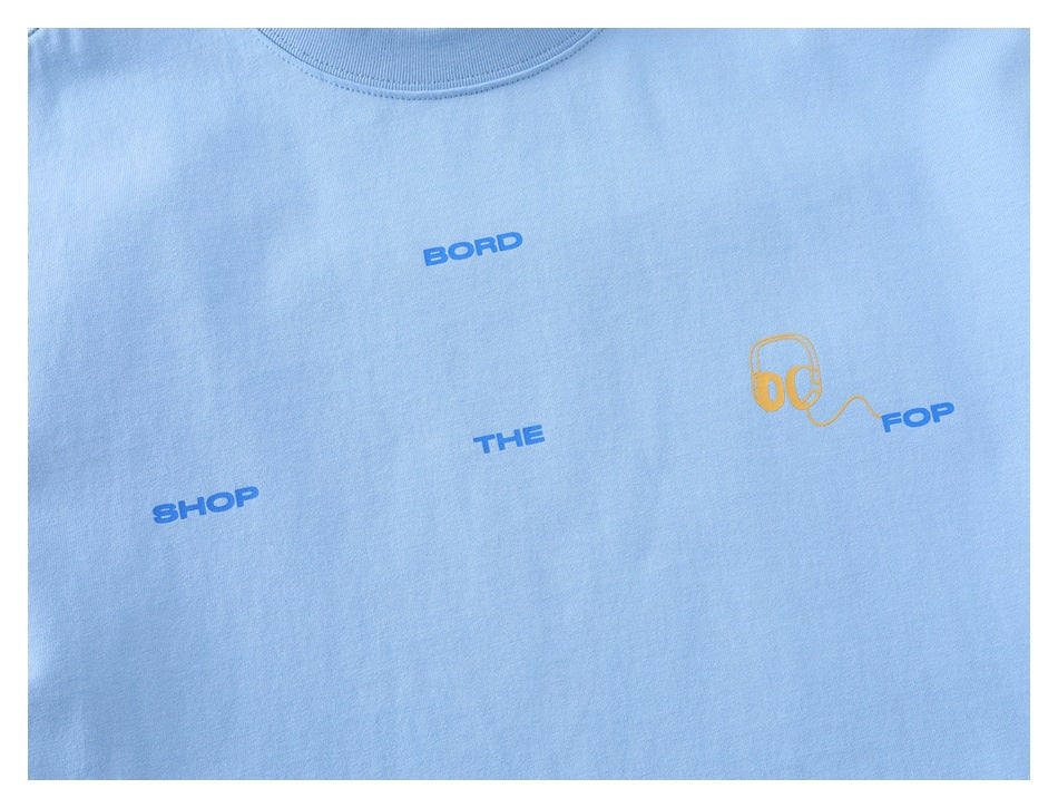Close-up of the light blue T-shirt chest graphic with blue lettering and a yellow headphones illustration.