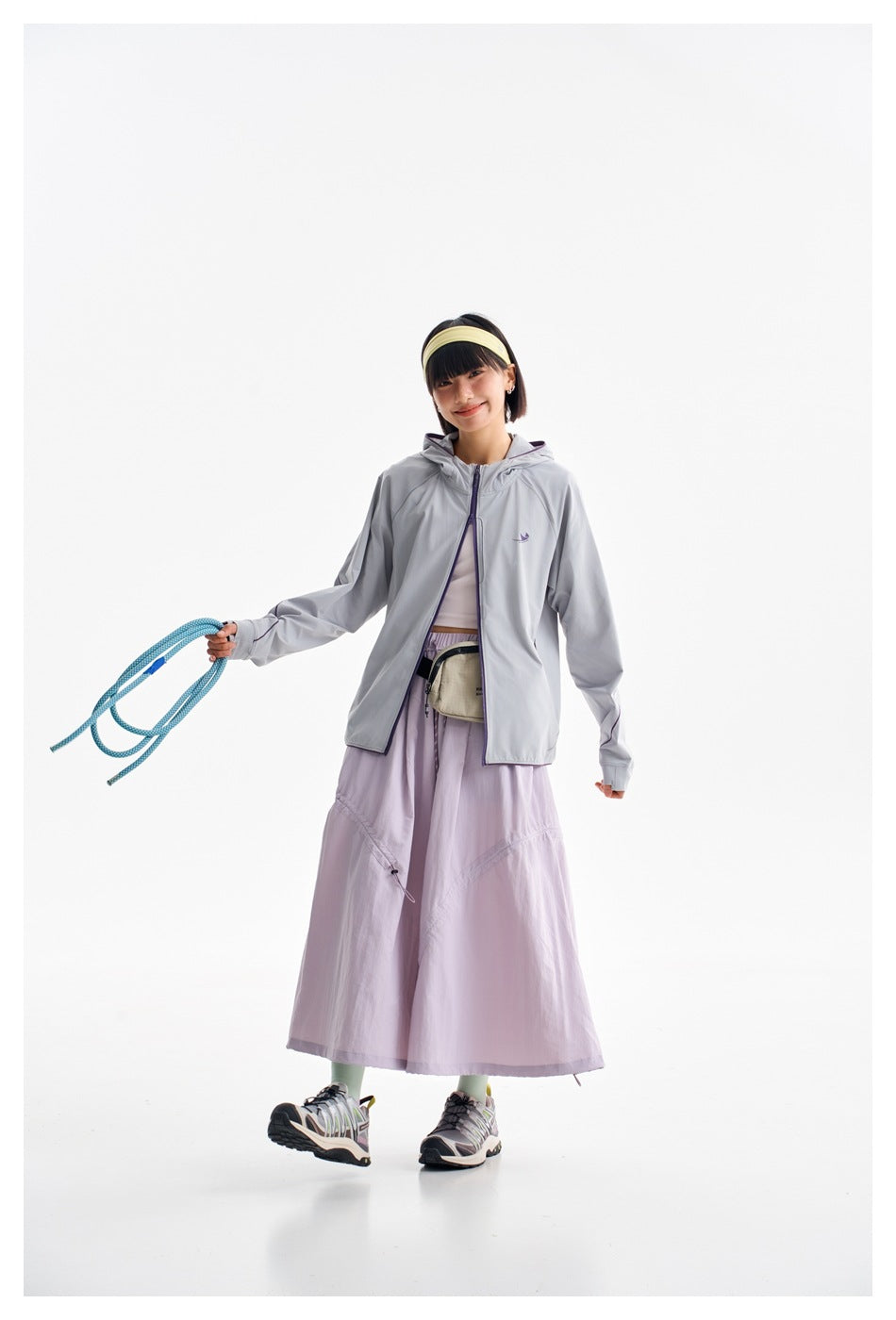 Woman wearing a light gray hooded zip jacket with purple trim and a pale lavender long skirt.