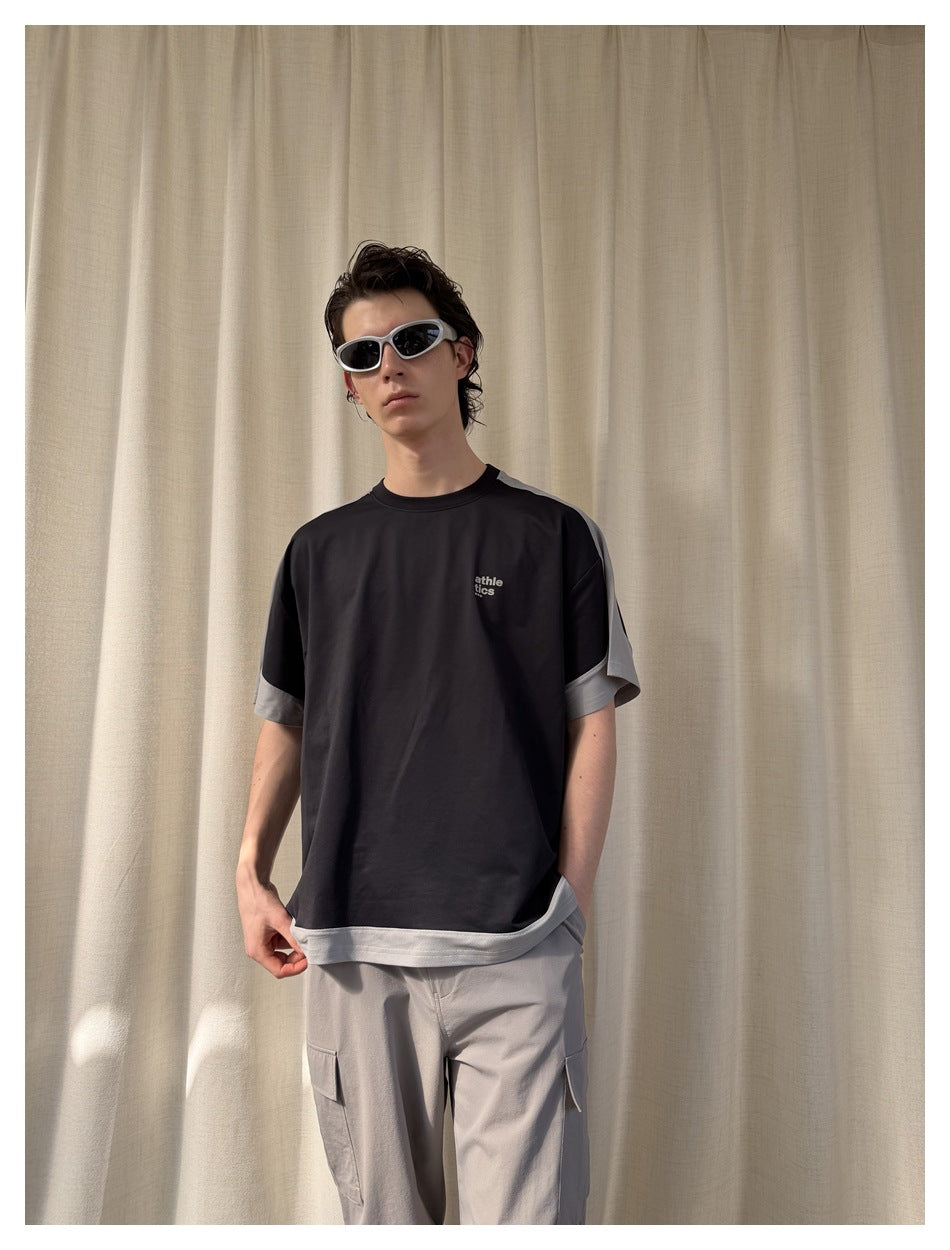 Model wearing a black T-shirt with gray contrast sleeves and hem, paired with gray cargo pants.