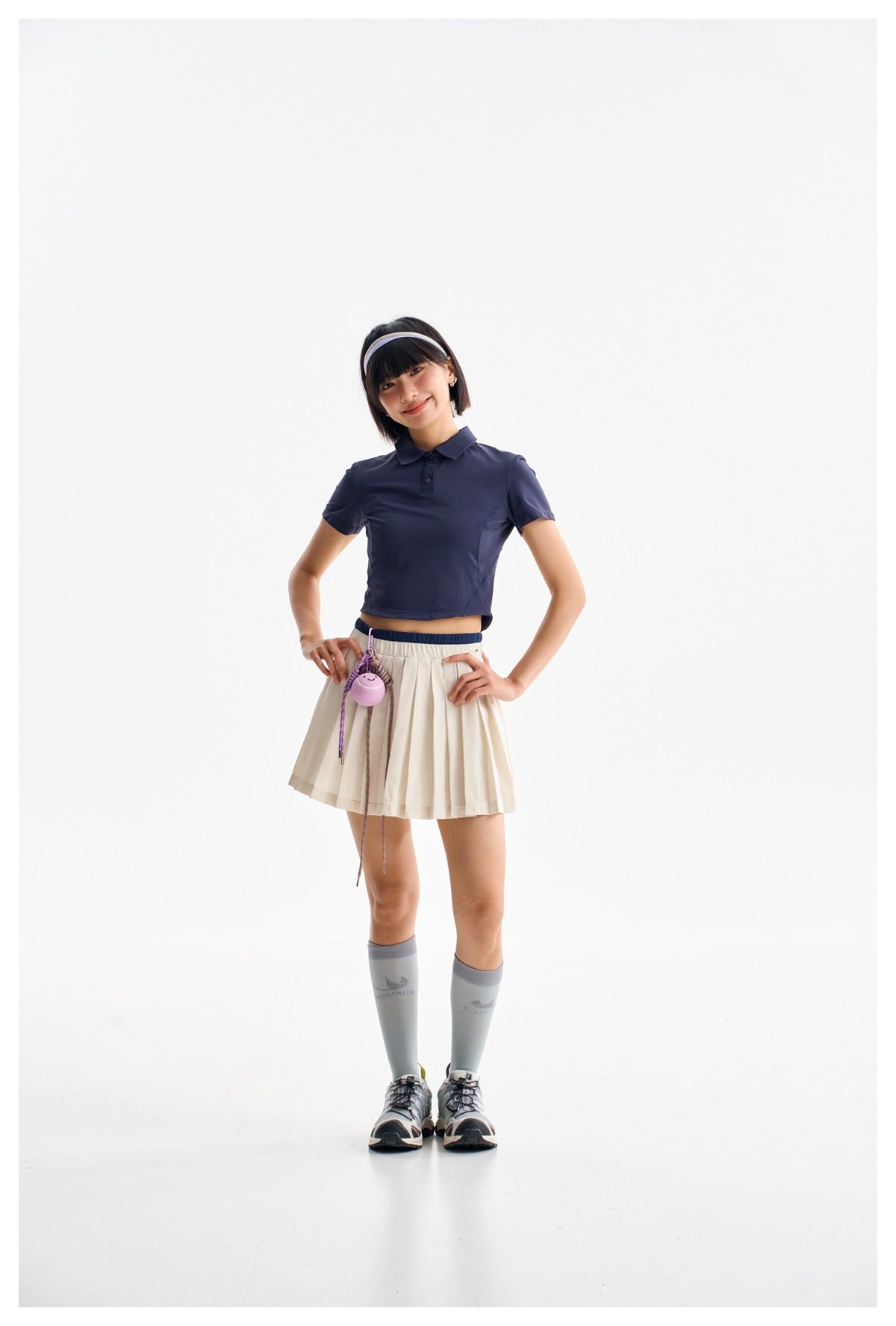Model wearing a navy cropped polo shirt and a cream pleated skirt.