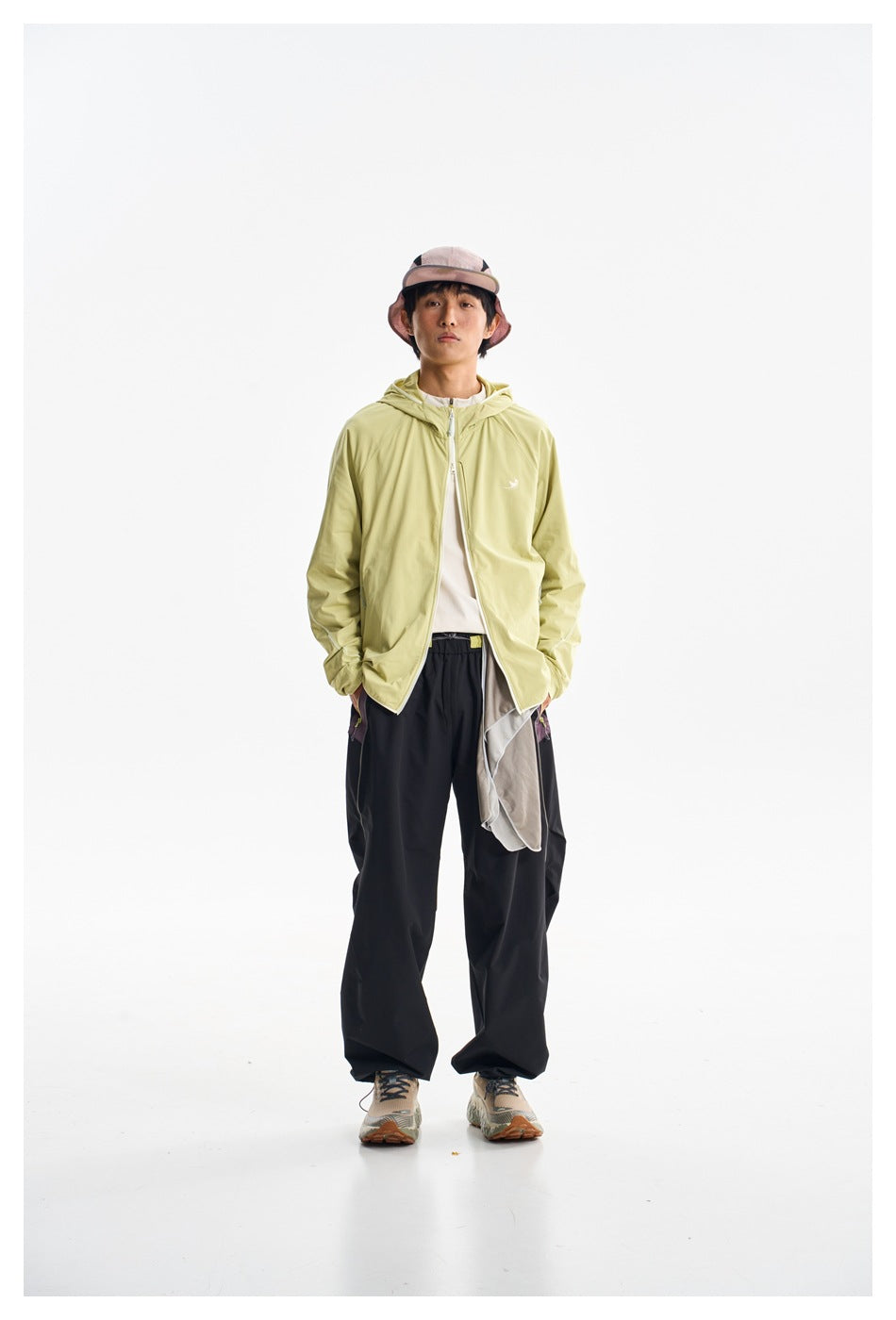 Model wearing a light yellow-green hooded zip jacket and loose black pants, shown from the front.