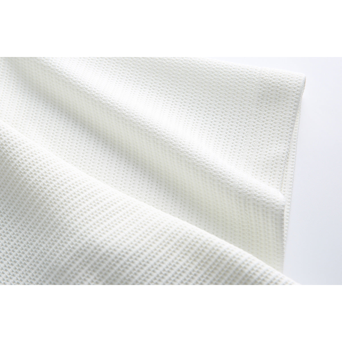 Close-up of white textured knit fabric with a finished edge.