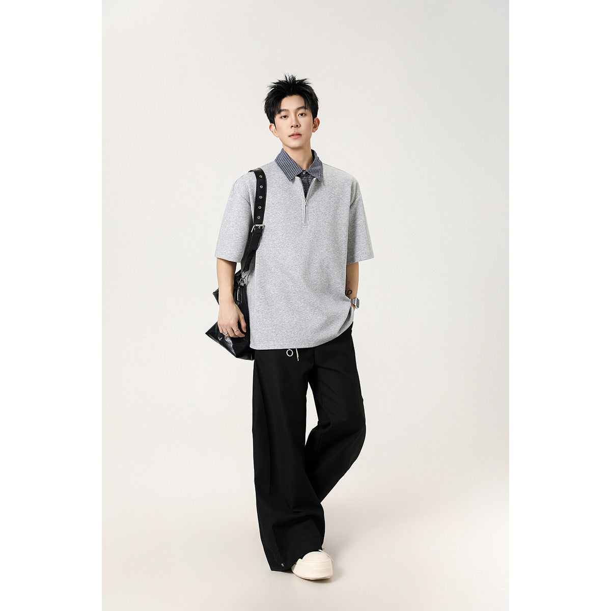 Model wearing a light gray short-sleeve quarter-zip polo with a checked collar and black wide-leg trousers.