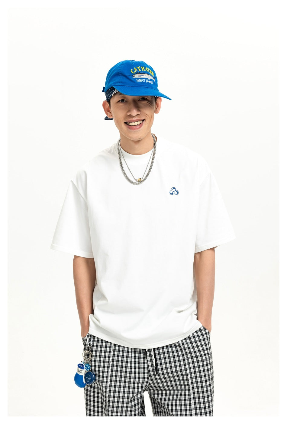 Model wearing a white short-sleeve tee with a small blue chest emblem and black-and-white checked trousers.
