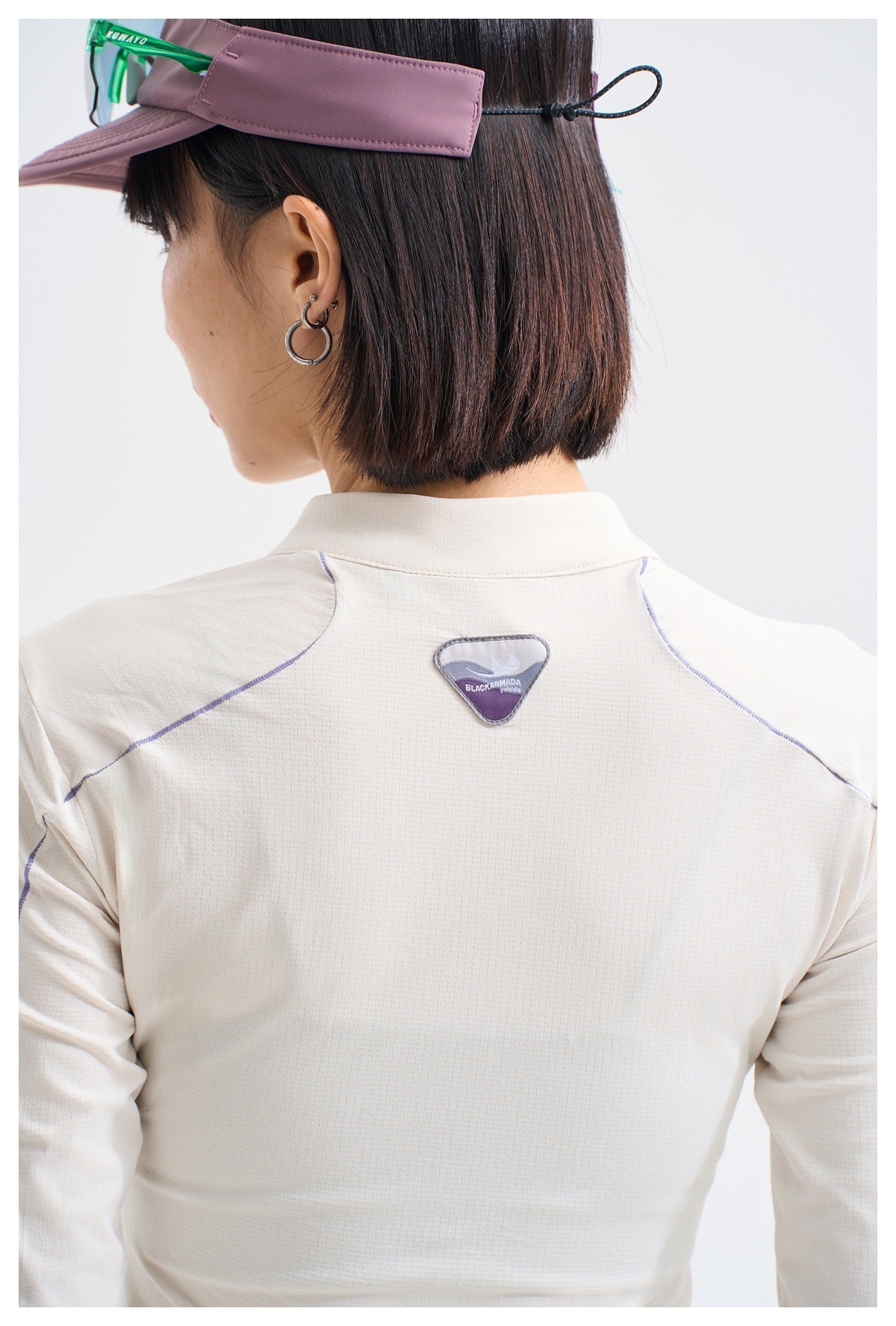 Back view of a model wearing a white long-sleeve top with purple seam lines and a small triangular upper-back patch.