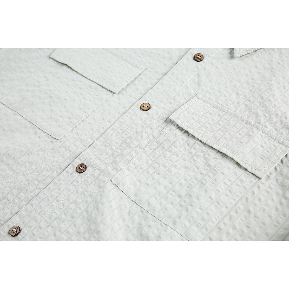 Close-up of a white shirt front with textured stripes, brown buttons, and flap chest pockets.