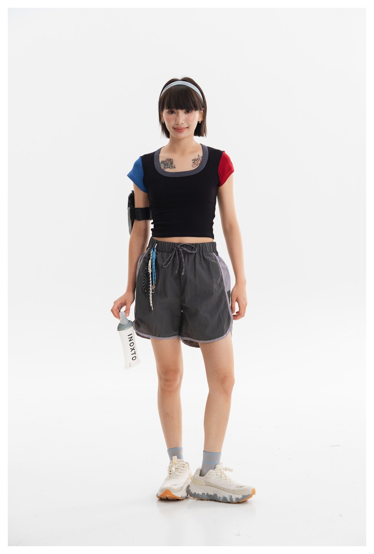 Model wearing a black cropped top with blue and red sleeves and charcoal running shorts with lavender trim.
