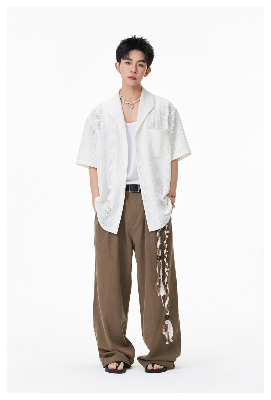 Full-length model wearing a white openwork short-sleeve shirt with a shawl collar and chest pocket, brown trousers, and