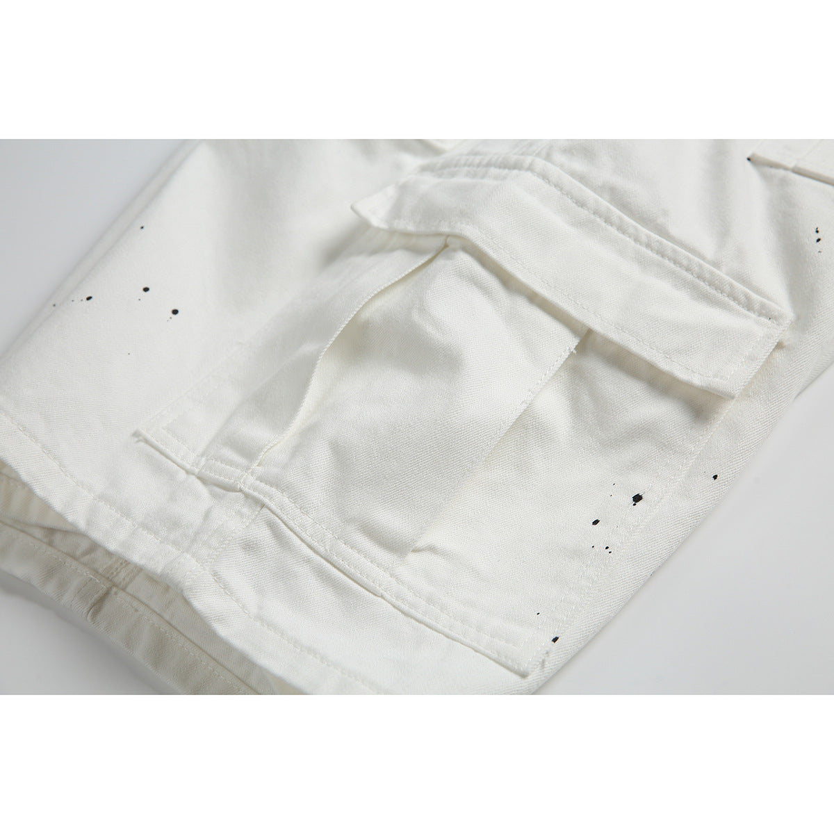 Close-up of a flap cargo pocket and black specks on white pants.