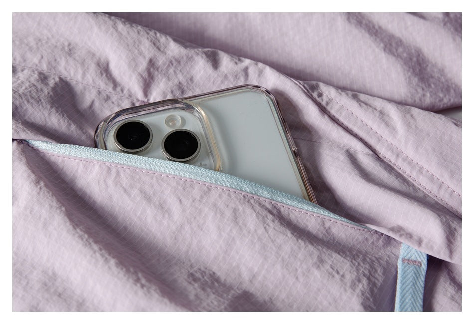 A phone tucked into a light-blue-zippered pocket on a pale lavender jacket.