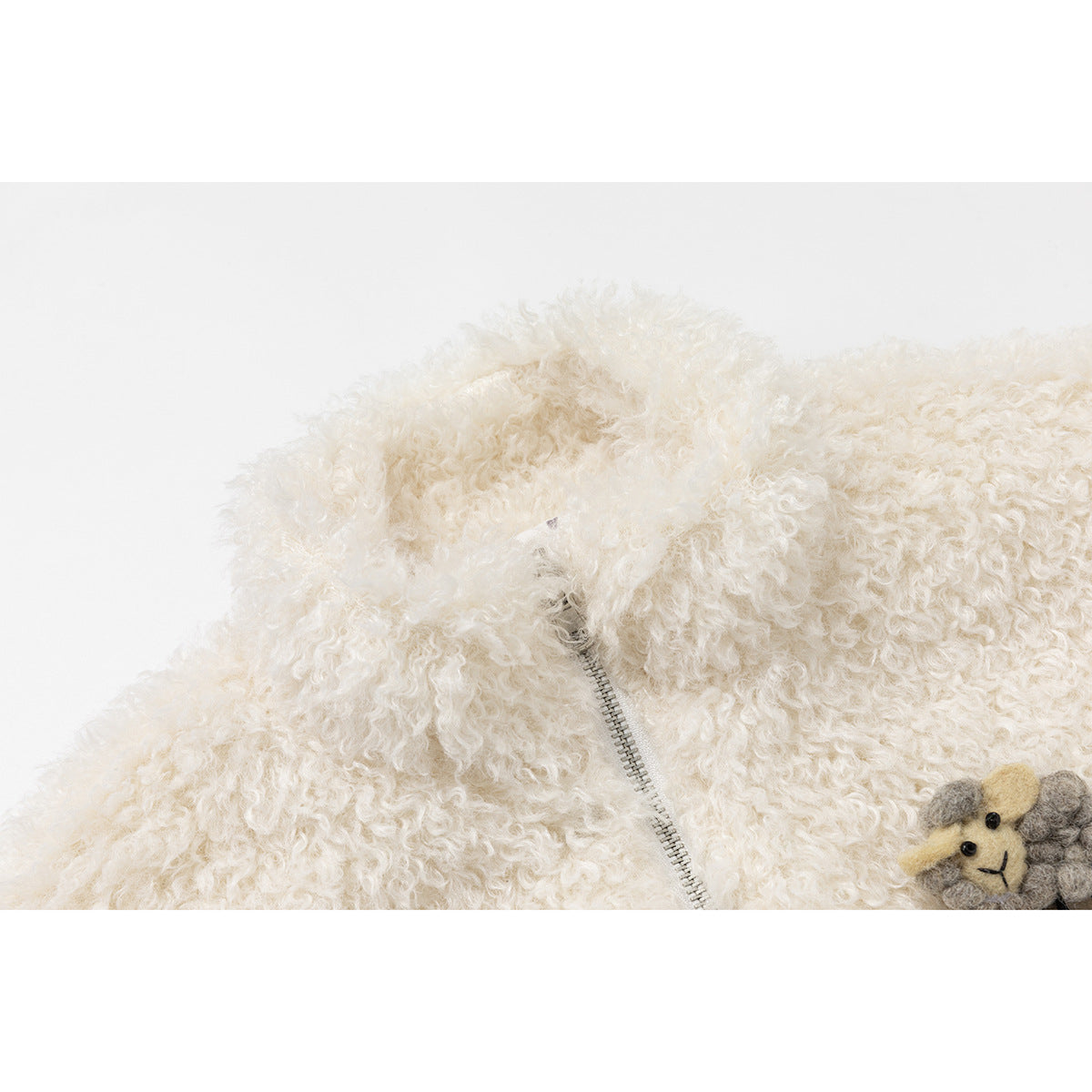 Close-up of an ivory curly-fleece vest with a silver zipper and part of a small sheep applique.
