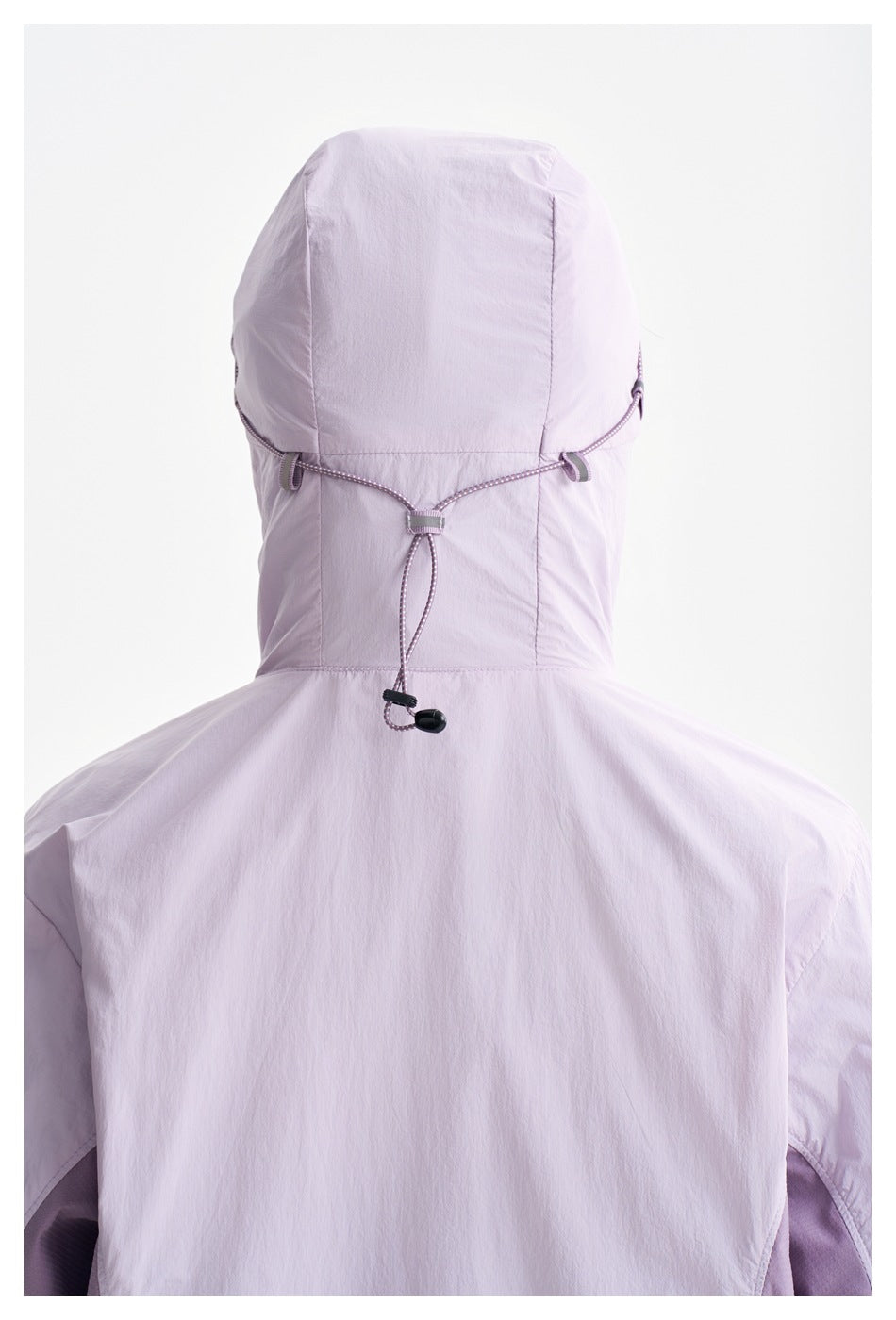 Rear view of a person wearing a pale lavender hooded jacket, showing the adjustable cord across the back of the hood.