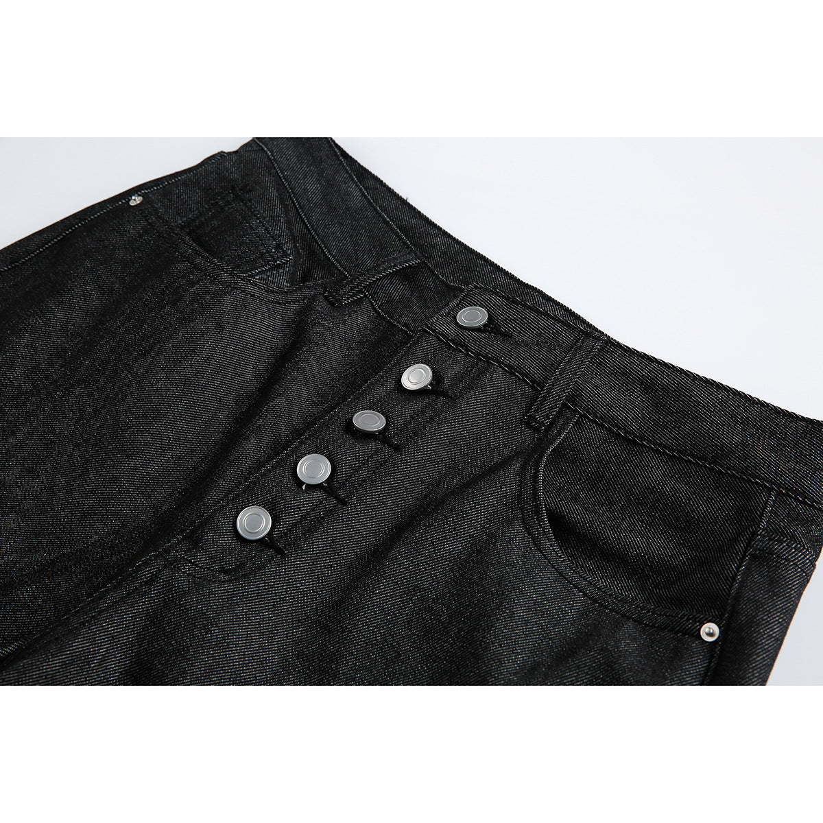 Close-up of black denim shorts showing the waistband, front pockets and silver button fly.