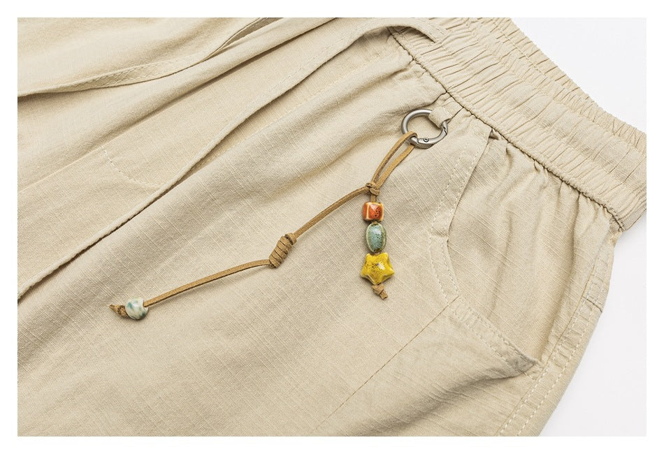 Close-up of beige bottoms with a dangling cord charm featuring small colorful beads beside the pocket and elastic waist.